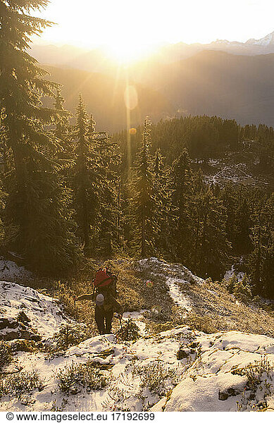 Backpacker hikes up mountain ridge during sunet.