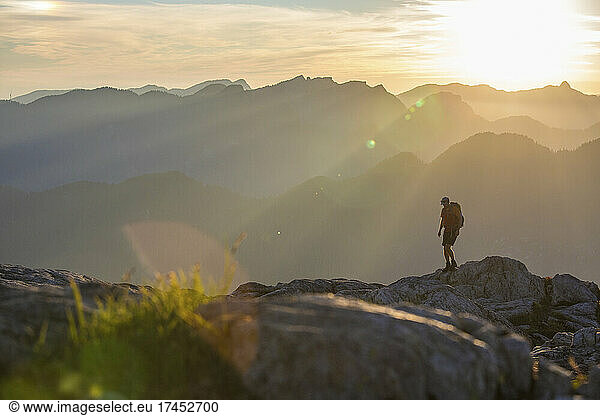 Backpacker hiking on rocky ridge  sunset mountain layers behind.