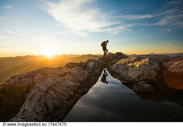 Backpacker hiking over rocky mountain terrain at sunset.