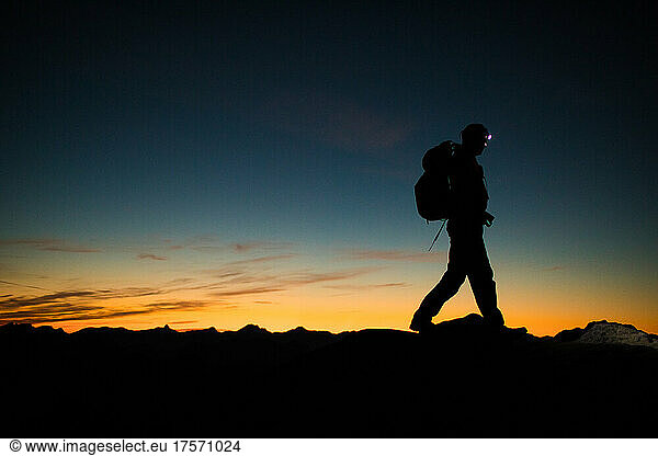 Backpacker hiking ridge at night via headlamp.