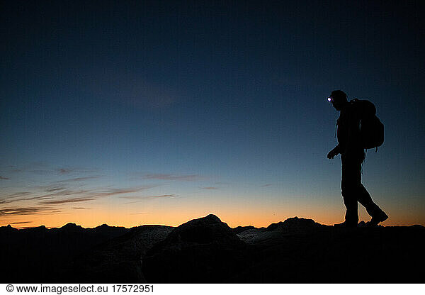 Backpacker navigates mountain ridge via healamp at night.