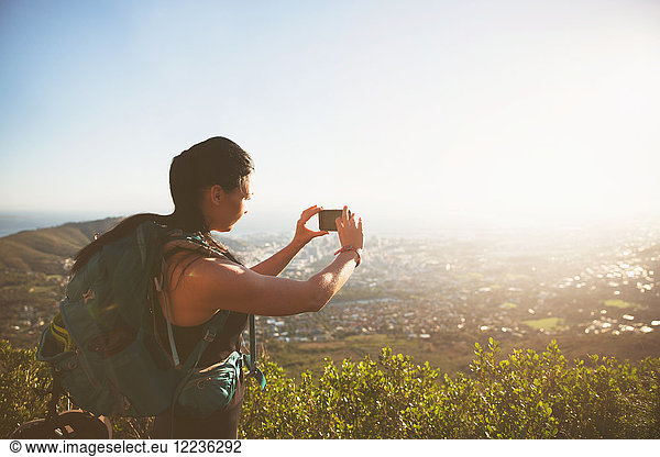Backpackerin mit Fotohandy fotografiert sonnige Stadtansicht