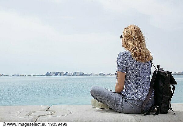 Backview of a blond woman sitting and watching the sea