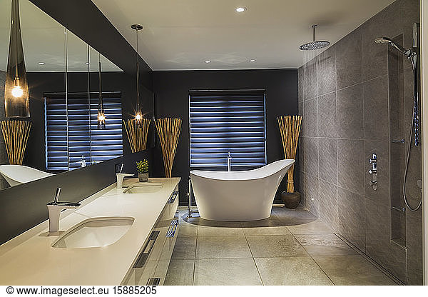 Badezimmer mit cremefarbenem Fliesenboden  braun gefliesten Wänden  cremefarbenem Doppelhandwaschbecken und weißer freistehender Badewanne.