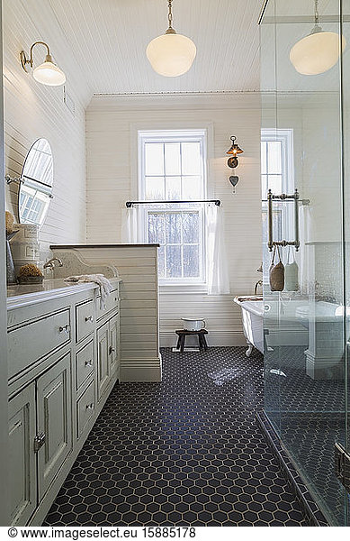 Badezimmer mit schwarzem Fliesenboden  creme getäfelten Wänden und Schiebefenstern. Freistehende weiße Badewanne und Glasduschkabine.