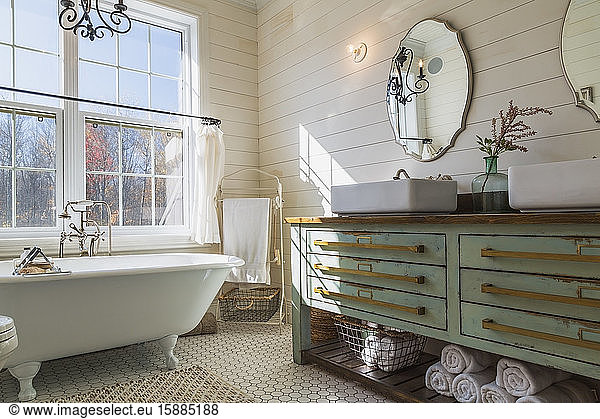 Badezimmer mit weißer Rollladenbadewanne  cremefarbener Fliesenboden und holzvertäfelten Wänden  grüner Waschtischunterschrank mit doppeltem Handwaschbecken.