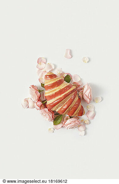 Baked croissant amidst rose petals against white background