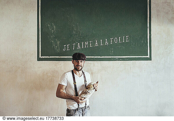 Baker holding country bread in front of wall with French text