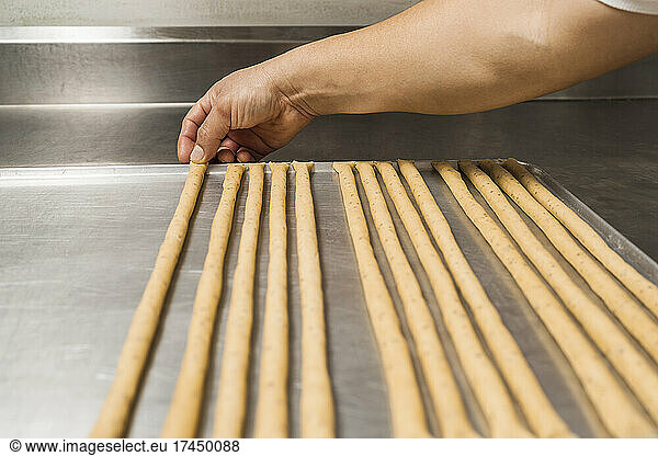 Baker stretching uncooked bread to make strips of artisan bread