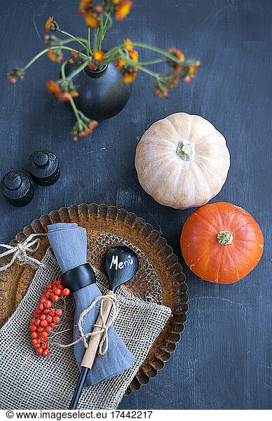 Baking pan  wooden spoon  weights  vase with wildflowers  rowanberries and pumpkin lying on black table