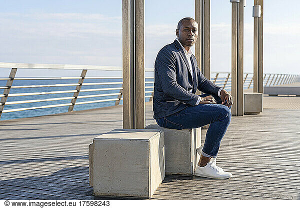 Bald businessman wearing smart casual sitting on bench at promenade