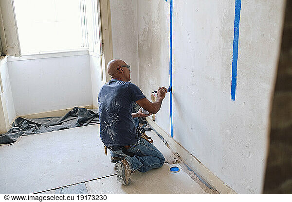 Bald construction worker painting on wall