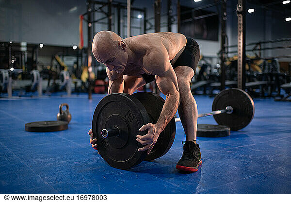 Bald elderly sportsman preparing barbell for training