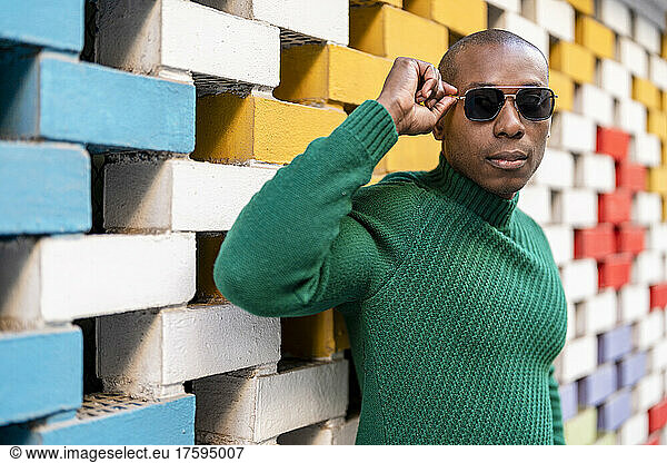 Bald man wearing sunglasses by multi colored brick wall
