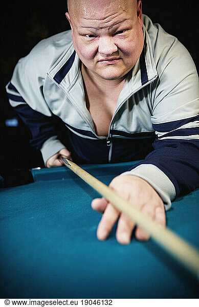 Bald man with cue stick leaning over a billiards table.