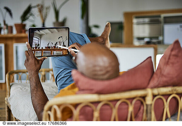 Bald man with digitized pen using tablet PC lying on sofa at home