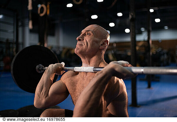 Bald senior sportsman squatting with heavy barbell