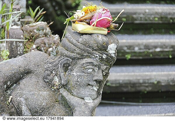 Balinesische religiöse Opfergabe (canang sari) über einer Steinstatue