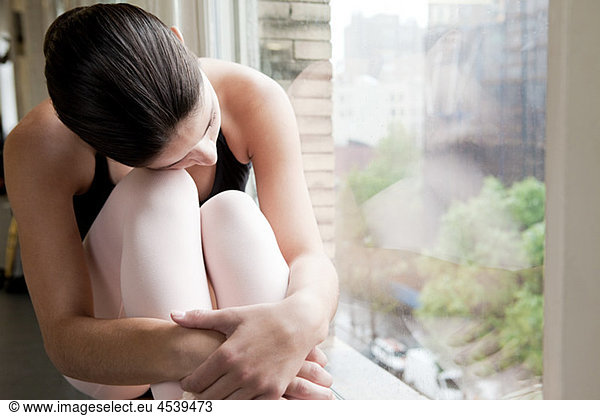 Ballerina by window  hugging her knees
