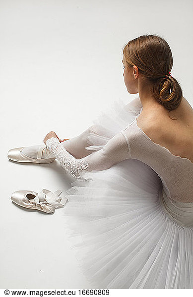 ballet dancer tying her ballet shoes around her ankle on white floor