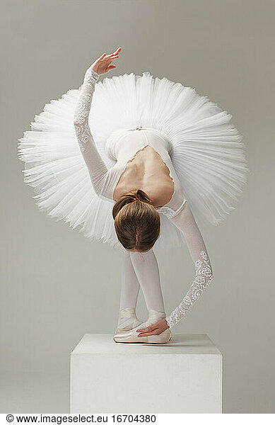 Balletttänzerin in weißem Ballett-Tutu verbeugt sich auf Podest  isoliert grau