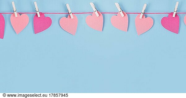 Banner with Valentines Day pink paper hearts hanging from line with pegs with empty copy space on blue background