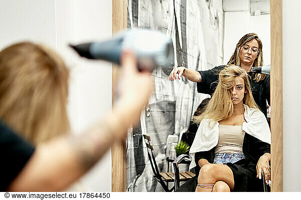 Barber blowing out clients hair after hair cut in barber shop