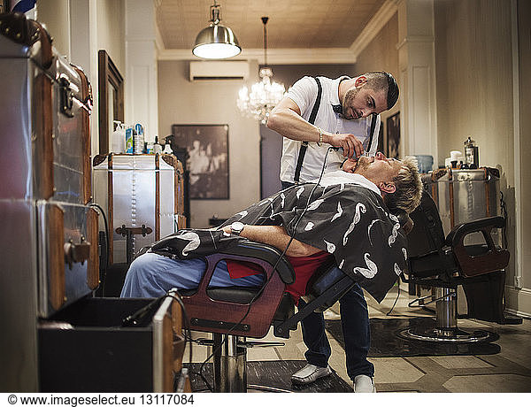 Barber shaving man's beard in shop