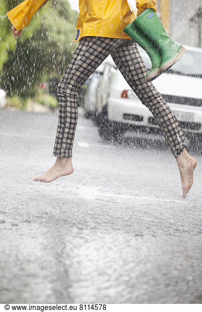 Barefoot woman running across street in rain