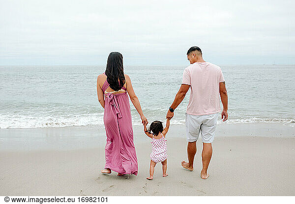 Barfüßige Eltern mit Kleinkind gehen am Strand Richtung Meer