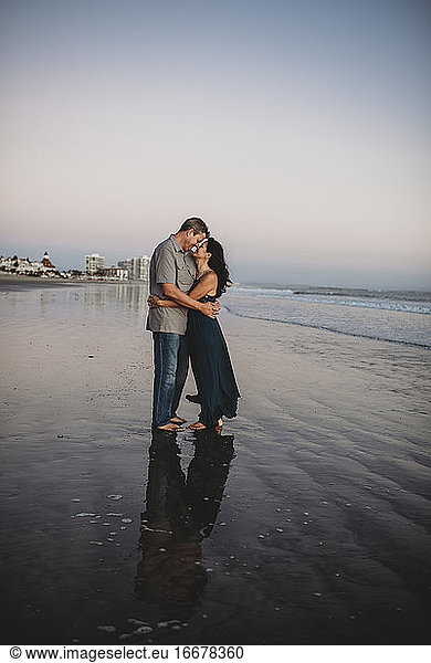 Barfuß liebendes Paar Mitte 40 am Strand  das sich von Angesicht zu Angesicht umarmt