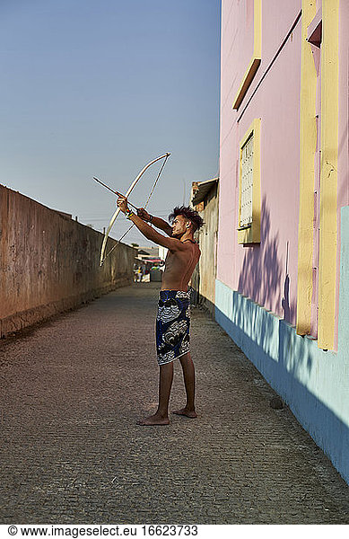 Barhäuptiger junger Mann mit Pfeil und Bogen im Freien