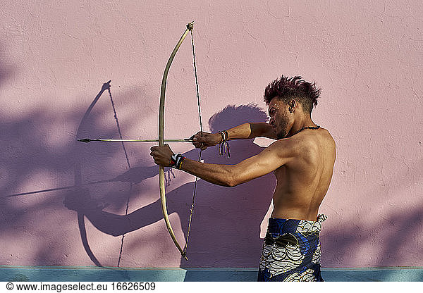 Barhäuptiger junger Mann mit Pfeil und Bogen im Freien
