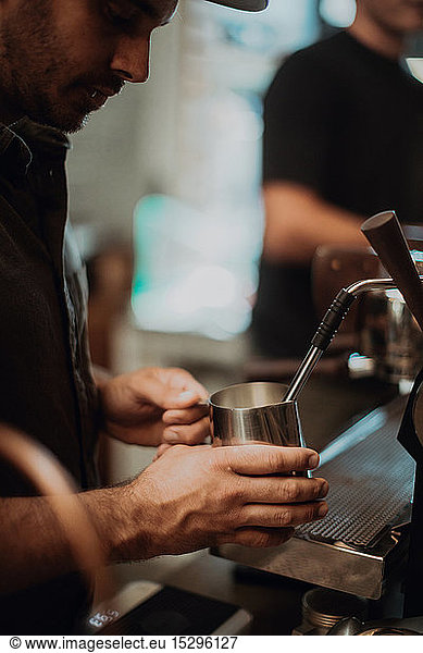 Barista erhitzt Milchkännchen auf Kaffeemaschine im Café  abgeschnittener flacher Fokus
