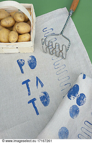 Basket of raw potatoes  potato masher and fabric covered in blue prints