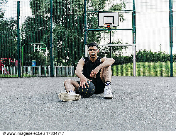 Basketballspieler mit Ball auf dem Spielfeld sitzend