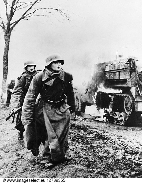 BATTLE OF THE BULGE  c1944. German troops passing by a burning US Army vehicle as the German infantry advanced during the Battle of the Bulge  possibly in Poteau  Belgium. Photograph  1944 or 1945.