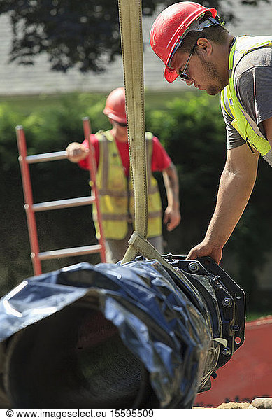 Bauarbeiter benutzt einen Gurt am Bagger  um einen Abschnitt der Wasserleitung zu führen