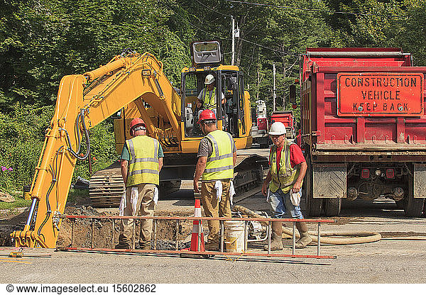 Bauarbeiter beobachten Bagger  die bei einem Wasserleitungsprojekt ein Loch graben