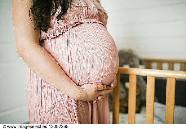 Bauchberührung in der Mitte einer schwangeren Frau  die zu Hause an der Krippe steht