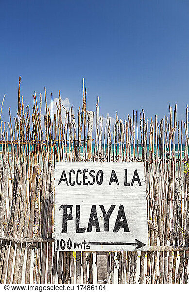 Beach access sign in Spanish  on a fence by the beach