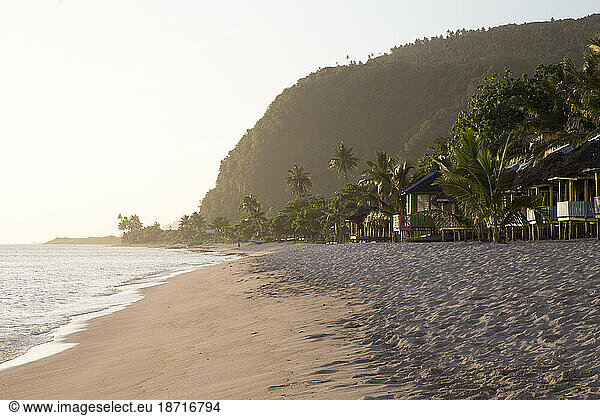 Beach huts & sandy beach with palm trees during golden hour