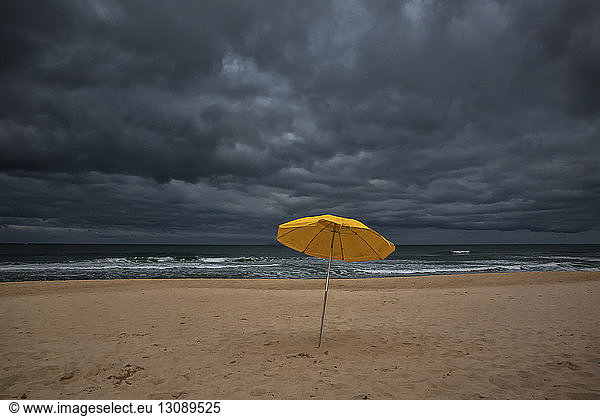 Beach umbrella on sand by sea against storm clouds