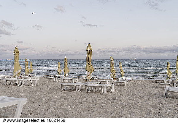 Beach umbrellas and deck chairs on empty beach at dusk