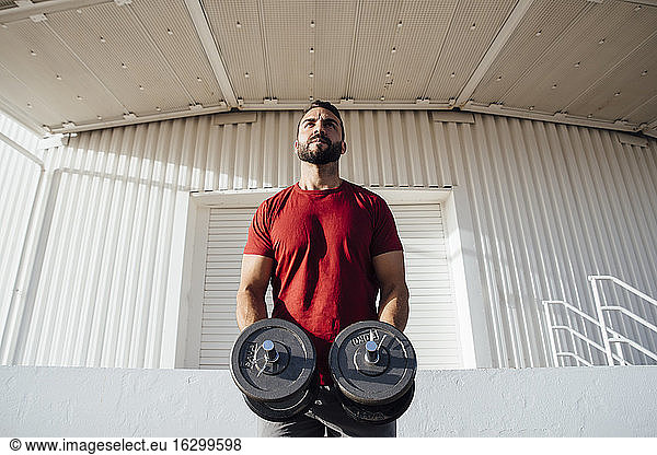 Beard man holding dumbbell while standing at street in city