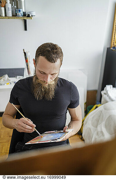 Beard man sitting with color palette in living room