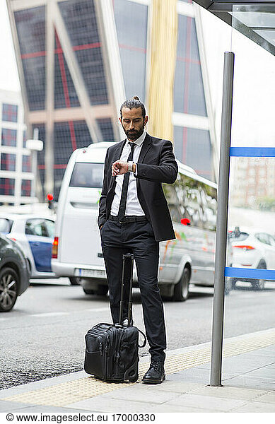 Bearded businessman checking time while waiting at bus stop