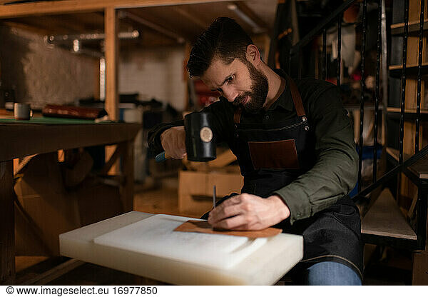Bearded craftsman making leather handicraft in cozy studio