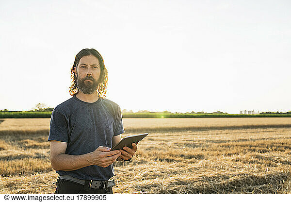 Bearded farmer with tablet PC standing at farm on sunny day