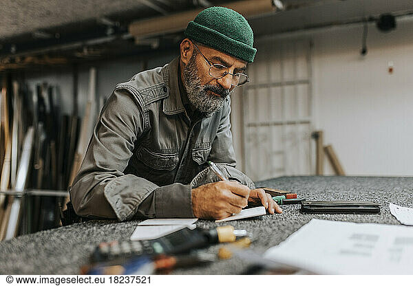 Bearded male entrepreneur wearing eyeglasses while writing at workbench